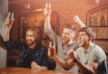 Cheerful friends men fans watch sports match on TV and drink draft beer in bar pub