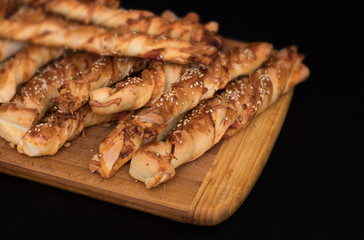 twisted cheese bread sticks with ham and sesame seeds on a wooden board on a black background
