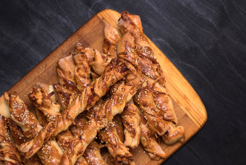 twisted cheese bread sticks with ham and sesame seeds on a wooden board on a black background