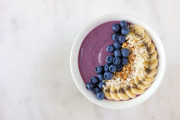 Healthy blueberry smoothie bowl with coconut, bananas, chia seeds and granola. Top view on a bright...