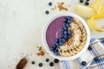 Healthy blueberry smoothie bowl with coconut, bananas, chia seeds and granola. Top view table scene...