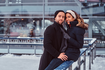 Young couple in love, date at the ice rink, a girl sitting on a guardrail and embracing with her...