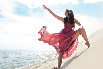 Woman in red waving dress with flying fabric runs on background of dunes.