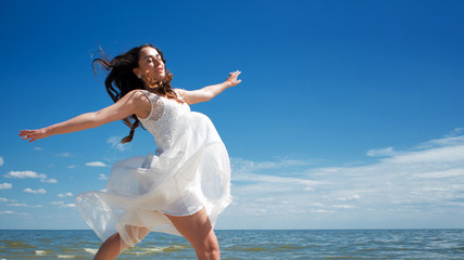 Young beautiful jumping brunette woman in white dress