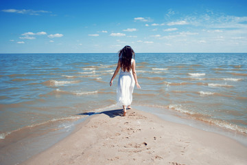 Fototapeta na wymiar Young beautiful brunette woman in white dress on the seashore.