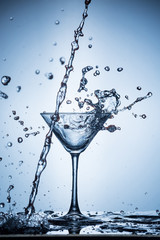 Splashing water on blue background. Cocktail glass with water.