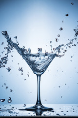 Splashing water on blue background. Cocktail glass with water.