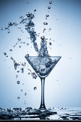 Splashing water on blue background. Cocktail glass with water.