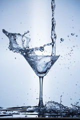 Fototapeta na wymiar Splashing water on blue background. Cocktail glass with water.