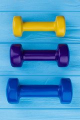 Three colorful dumbbells on wooden background. Yellow, purple and blue dumbbells on blue wood surface. Sport and fitness concept.