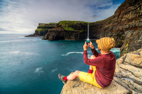 Man with smartphone snaps photos at Gasadalur waterfall, Vagar island, Faroe Islands, Denmark