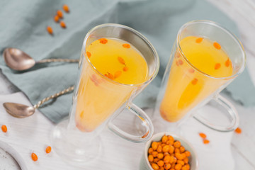 Two high glasses with colorful hot sea buckthorn tea with fresh sea buckthorn berries