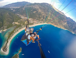 Paragliding in the sky. Paraglider tandem flying over the sea with blue water and mountains in...