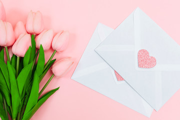 Female hands with a bouquet of pink tulips and blank white letter envelopes, on a pink background....