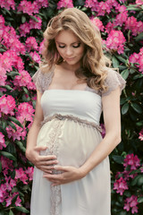 Beautiful pregnant woman outdoors on pink rhododendron flowers backround