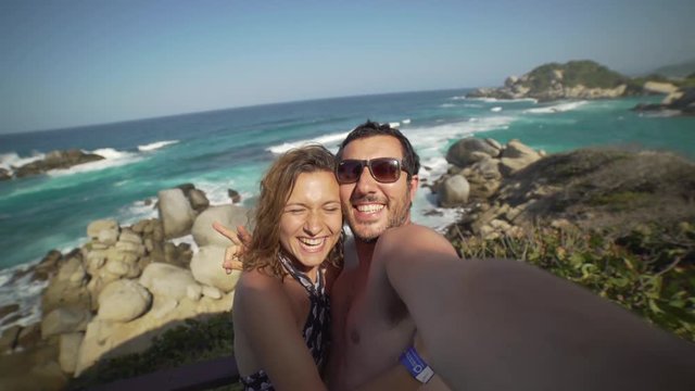 happy couple taking selfie photo in front of the sea in Tayrona National Park, Tropical Colombia. Crazy tourists travelling on the white beach of caribbean sea. 4K video