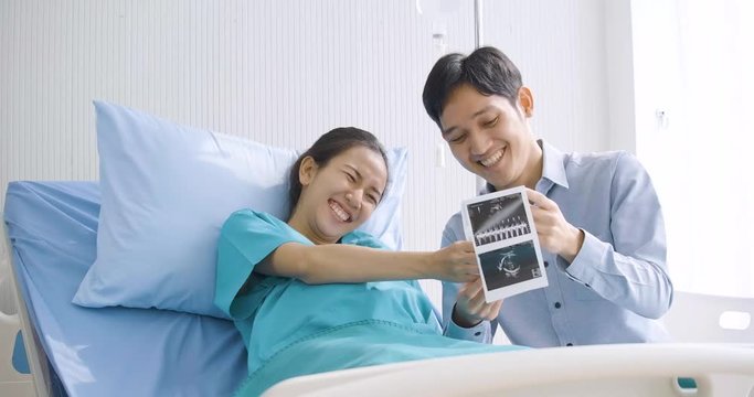 Lovely asian couple excited parents-to-be look at sonogram pictures.