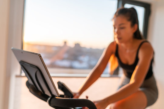 Home Fitness Fit Woman Exercising On Smart Stationary Bike At Home Gym Class Watching Screen Online Class Biking Exercise. Young Girl Training Spinning The Pedals Pedaling. Focus On Screen.