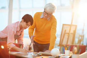 Portrait of mature art teacher working with female student in sunlit art studio, copy space
