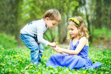 Brother and sister sit on the grass. Children's games, leisure. Two children are sitting on green meadow and smile. Boy and girl kiss on sunny day.