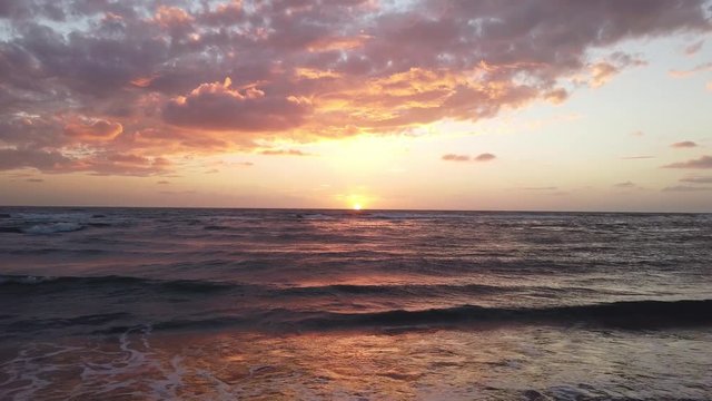 Awesome golden hour sunset at beach with fantastic sky with altocumulus stratiformis and ocean waves breaking on shoreline with sunbeams reflections on rough sea foamy water	