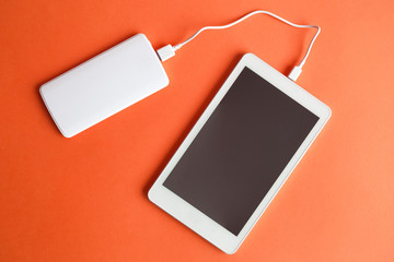 Digital tablet with external battery charger abstract isolated on orange.