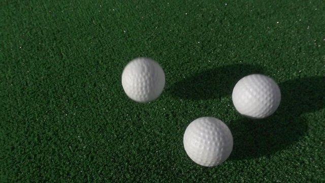 Sports and games. A slow motion close up of a three golf balls dropping and bouncing on artificial grass.