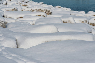 Fototapeta na wymiar Long line of rocks along Lake Michigan shoreline covered with frozen ice and snow on a sunny winter day.