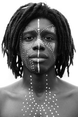 Portrait of young african man with dreadlocks and traditional face paint looking straight into the camera with a serious expression, black and white