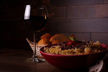 Pasta with meat Glass of wine, candle and bread all ready for romantic dinner on Valentine's day with wooden background