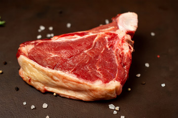 Raw meat steak with seasoning on concrete background. Beef T-bone steak, top view. Barbecue concept. Ingredients for roasting meat.