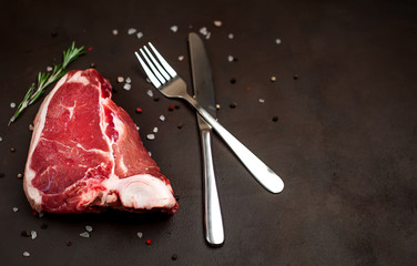 Raw meat steak with seasoning on concrete background. Beef T-bone steak, top view. Barbecue...