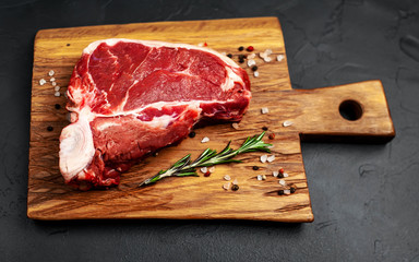 Raw meat steak with seasoning on a cutting board, background concrete. Space for text. Beef T-bone...