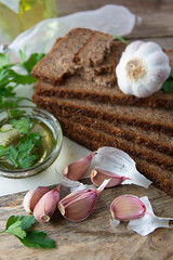 Sliced wholegrain bread wit seeds, greens, oil and garlic on cutting board. Carbohydrates.