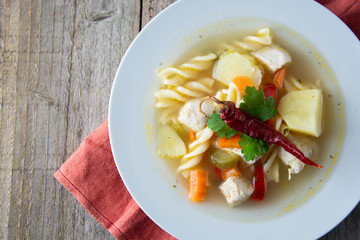 Chicken soup with noodles and vegetables, rustic wooden background. Healthy homemade food. Top view. Square iamge.