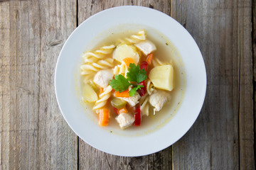 Chicken soup with noodles and vegetables, rustic wooden background. Healthy homemade food. Top view. Square iamge.