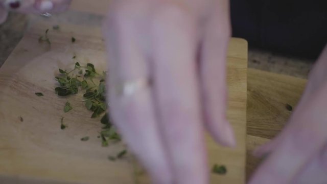 Closeup of a woman chopping thym herb on a wooden board in the kitchen.