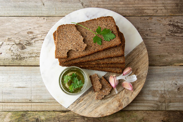 Sliced wholegrain bread wit seeds, greens, oil and garlic on cutting board. Carbohydrates. Top view.