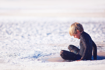young boy applying natural mineral mud on body at salt lake