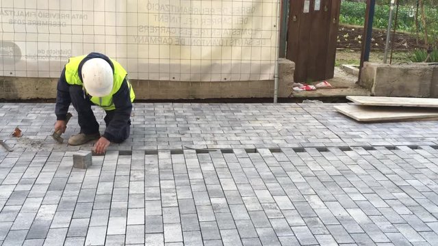 Public Ajuntament de Barcelona worker with hammer, helmet and yellow jacket positioning a square block of concrete on under construction pedestrian street or sidewalk