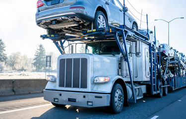Big rig car hauler semi truck transporting cars on two levels semi trailer driving on winter frosty...