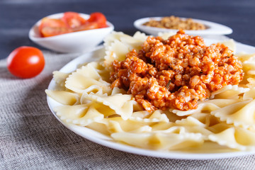Farfalle bolognese pasta with minced meat on black wooden background.