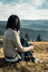 girl with a metal cup sits on a background of mountains