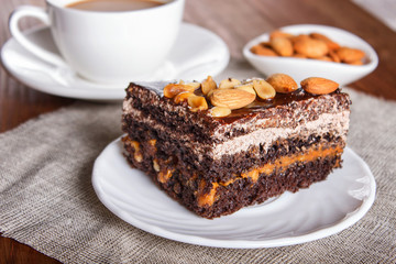 Chocolate cake with caramel, peanuts and almonds on a brown wooden background.