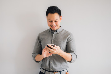 Happy smile face of handsome Asian man use smartphone stand isolated on gray background.