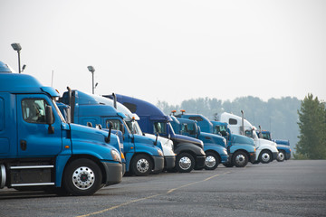 Profiles of different big rigs semi trucks standing in row on parking lot