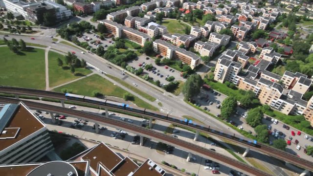 High wide view of the KTH Royal Institute of Technology campus in Kista. A bright blue train of the public transportation system entering the passenger station. Colorful modern university buildings.