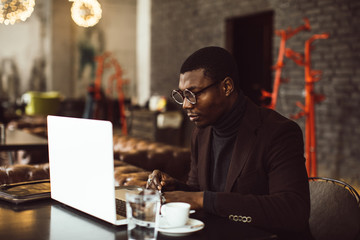 Portrait of happy african businessman working on laptop in a restaurant.
