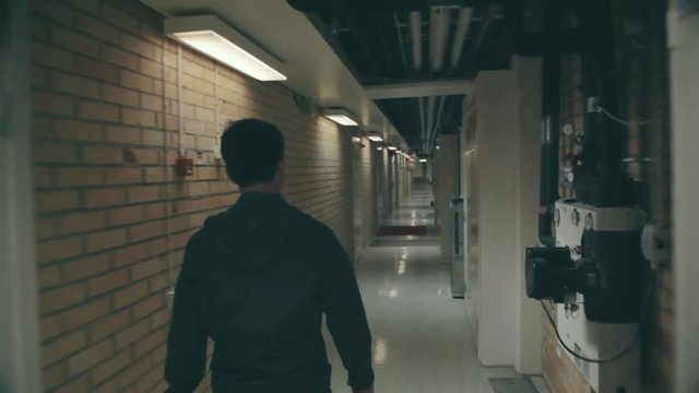 A man in silhouette walks down a long white dimly lit corridor in a building. White cabinets and doors line a hallway as a man walks alone. Industrial basement spooky setting. FOLLOW.