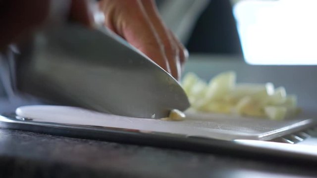 SLOWMO - Chef chopping garlic with knife on cutting board in kitchne of motorhome - Close Up